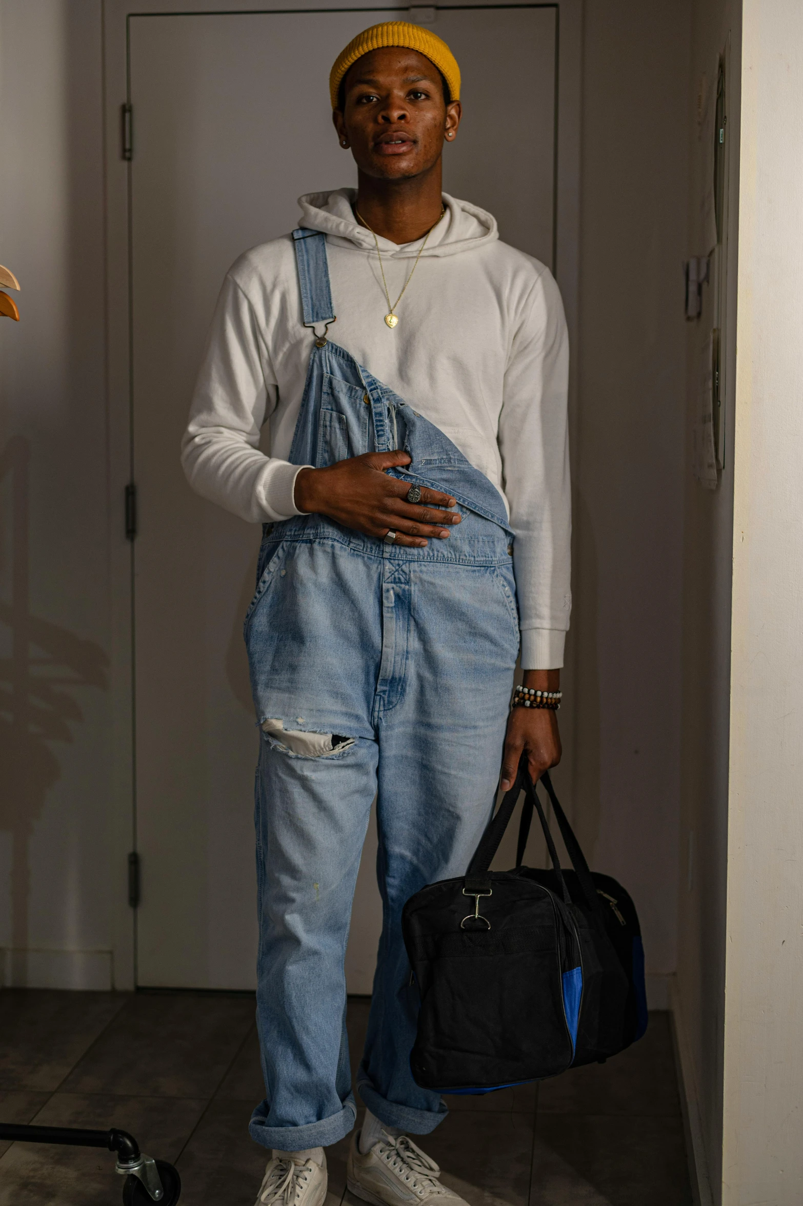 a man standing in a room holding a bag, featured on reddit, wearing blue jean overalls, black teenage boy, ☁🌪🌙👩🏾, portrait photo