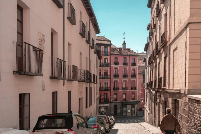a person walking down a narrow cobblestone street, inspired by Óscar Domínguez, pexels contest winner, hyperrealism, pink marble building, parking in the street, madrid, cars parked underneath
