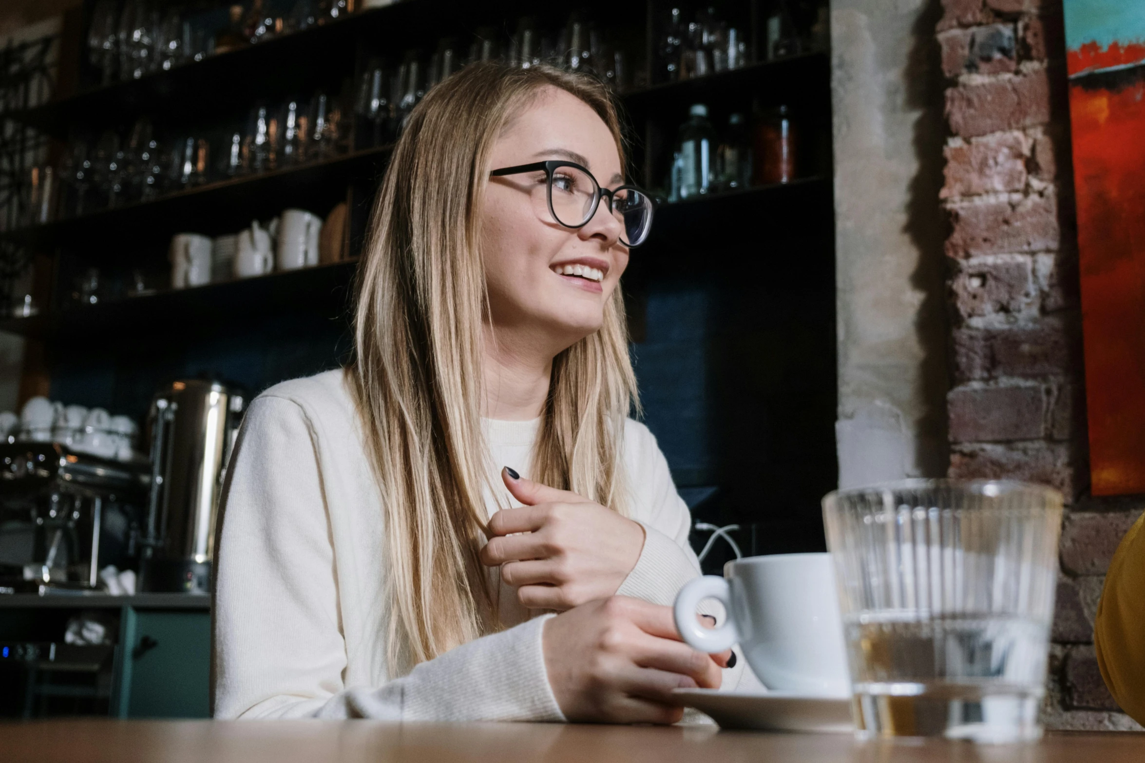 a woman sitting at a table with a cup of coffee, pexels contest winner, happening, girl wearing round glasses, avatar image, flirting smiling, mid shot photo