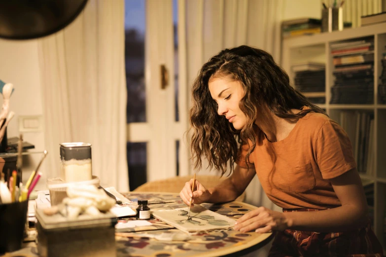 a woman sitting at a table with a magazine, a photorealistic painting, by Jakob Gauermann, pexels contest winner, drawing pictures on a notebook, intricate organic painting, in the evening, crafting