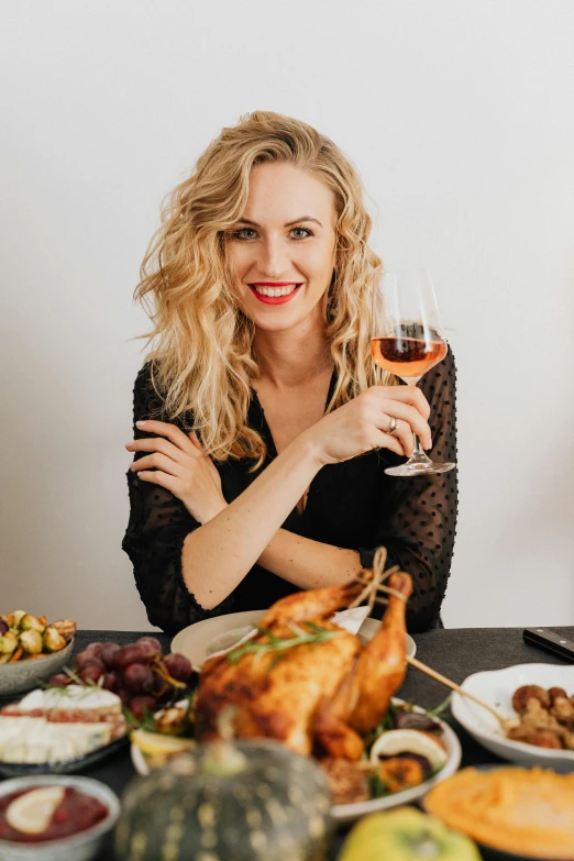 a woman sitting at a table with a glass of wine, food, cocky smirk, festive, blonde woman