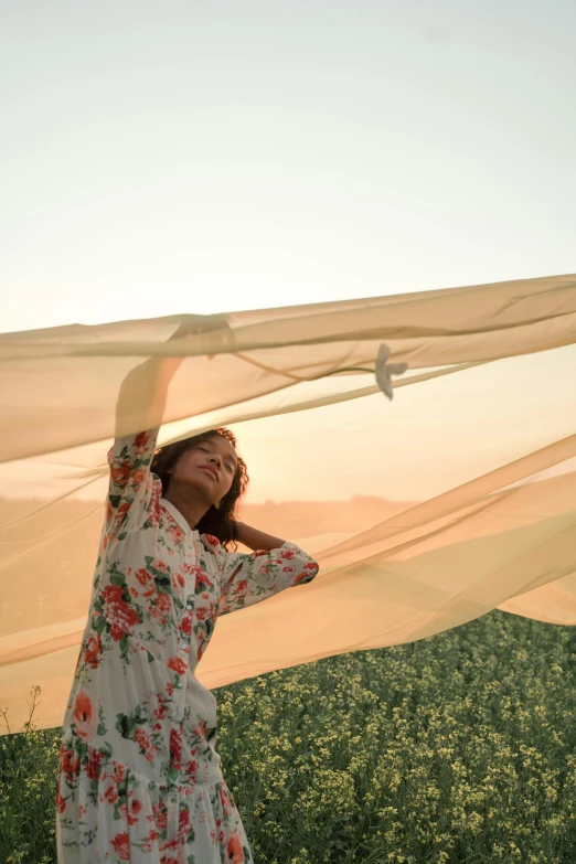 a woman standing on top of a lush green field, inspired by Christo, trending on unsplash, renaissance, soft translucent fabric folds, white cloth in wind shining, during sunset, canopy