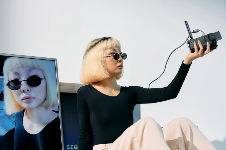 a woman sitting in front of a television holding a camera, video art, futuristic hairstyle, kda and sam yang, implanted sunglasses, girl making a phone call