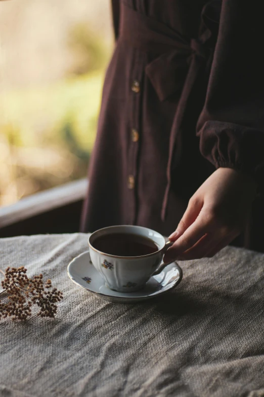 a woman holding a cup of coffee on a table, inspired by Elsa Bleda, cottagecore, brown, wide, chocolate