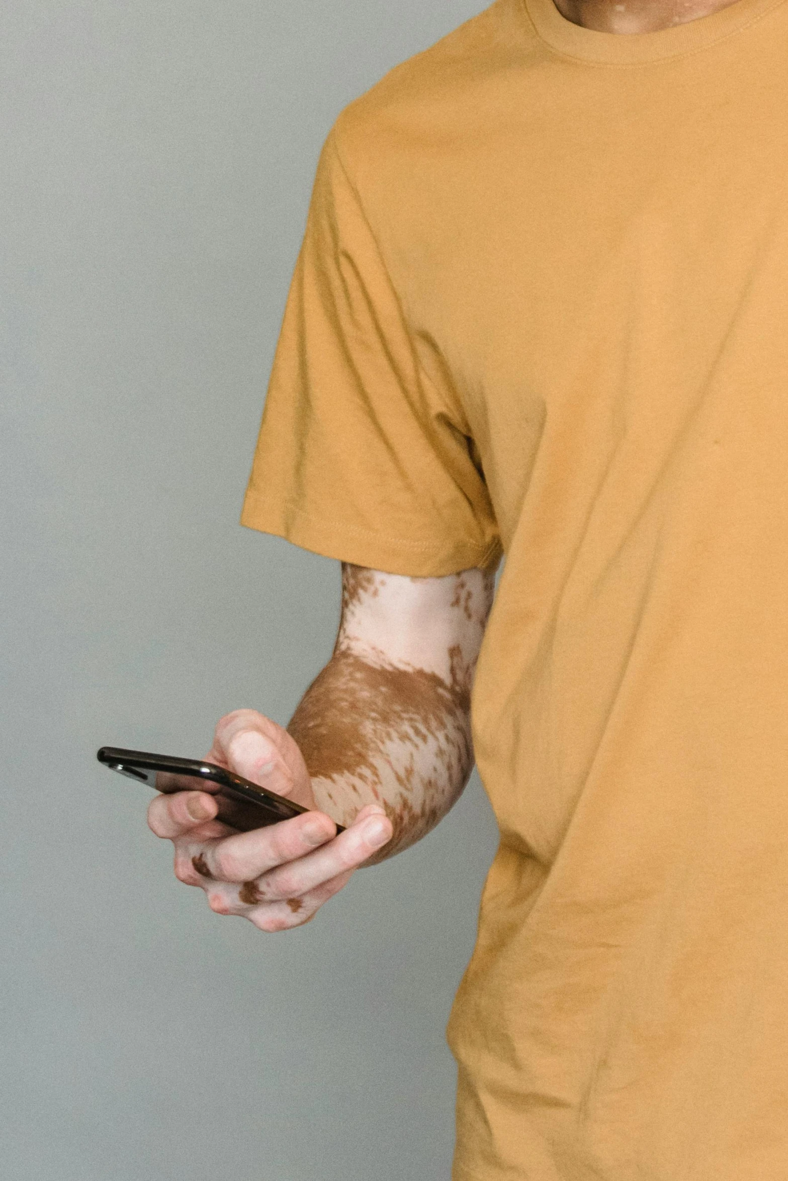 a man in a yellow shirt holding a cell phone, a tattoo, dirt - stained skin, veiny hands, 2019 trending photo, wearing a brown