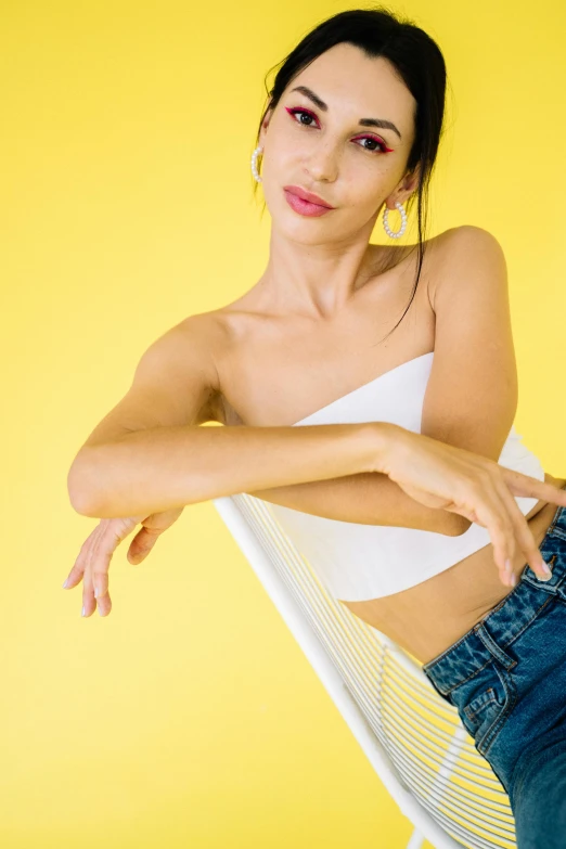 a woman sitting on top of a white chair, by Robbie Trevino, wearing yellow croptop, solid background, lulu chen, daisy dukes