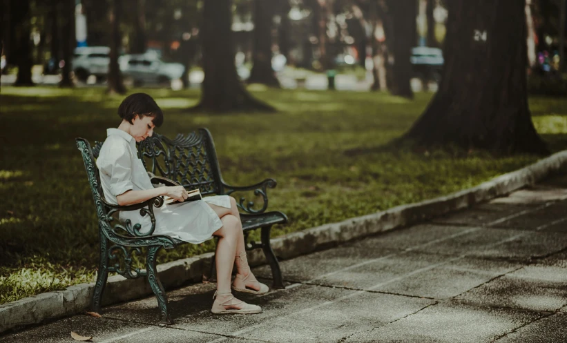 a person sitting on a bench reading a book, by Elsa Bleda, pexels contest winner, realism, young girl, square, green spaces, unhappy