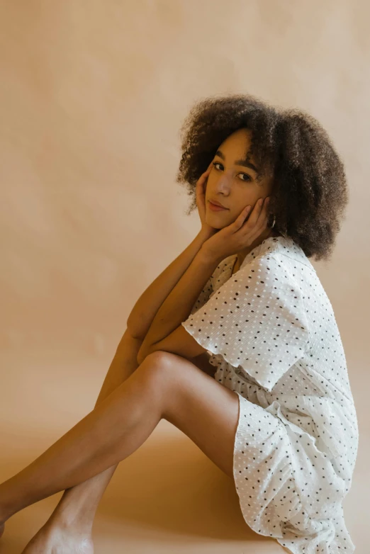 a woman sitting on the floor with her legs crossed, trending on pexels, antipodeans, curly bangs and ponytail, ashteroth, printed on a cream linen t-shirt, nightgown