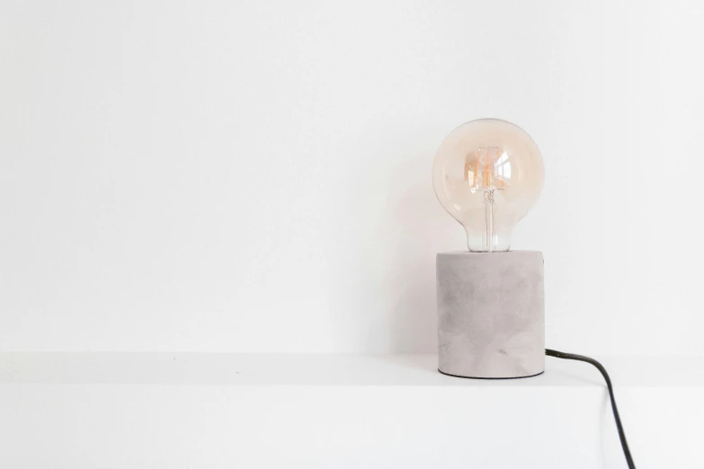 a light bulb sitting on top of a concrete block, inspired by Constantin Hansen, unsplash, minimalism, on a white table, natural soft rim light, made of concrete, medium height