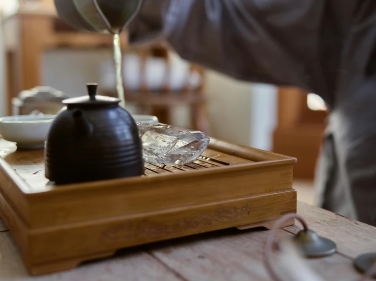 a person pouring tea into a cup on a tray, inspired by Kanō Shōsenin, half-frame square glasses, bamboo, grey, sichuan