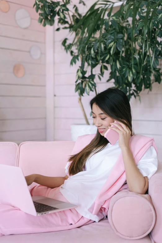 a woman sitting on a pink couch using a laptop, trending on pexels, girl making a phone call, white and pink cloth, mai anh tran, freezing