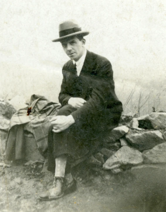 an old photo of a man sitting on a rock, inspired by Max Klinger, bauhaus, wearing a fedora, leonard cohen, florence harrison, he is at camp