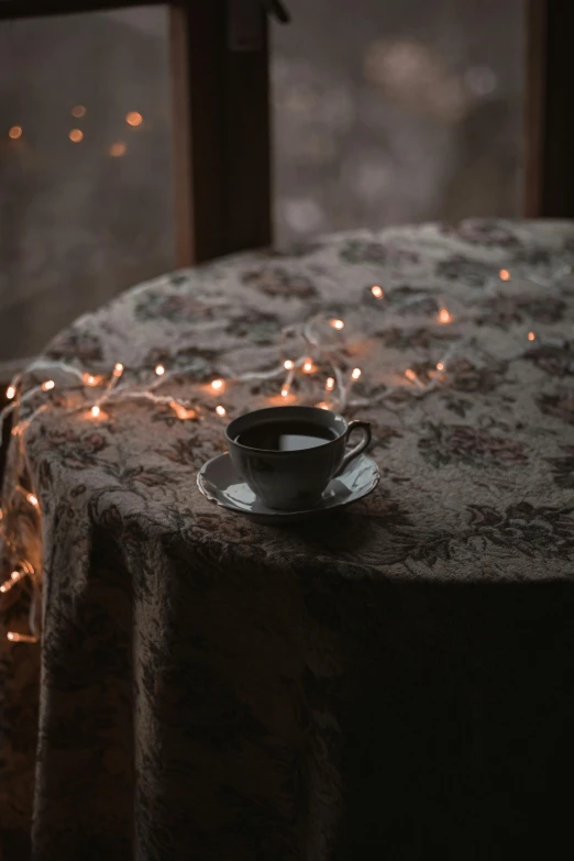 a cup of coffee sitting on top of a table, inspired by Elsa Bleda, pexels contest winner, romanticism, fairy lights, velvet tablecloth, black, brown