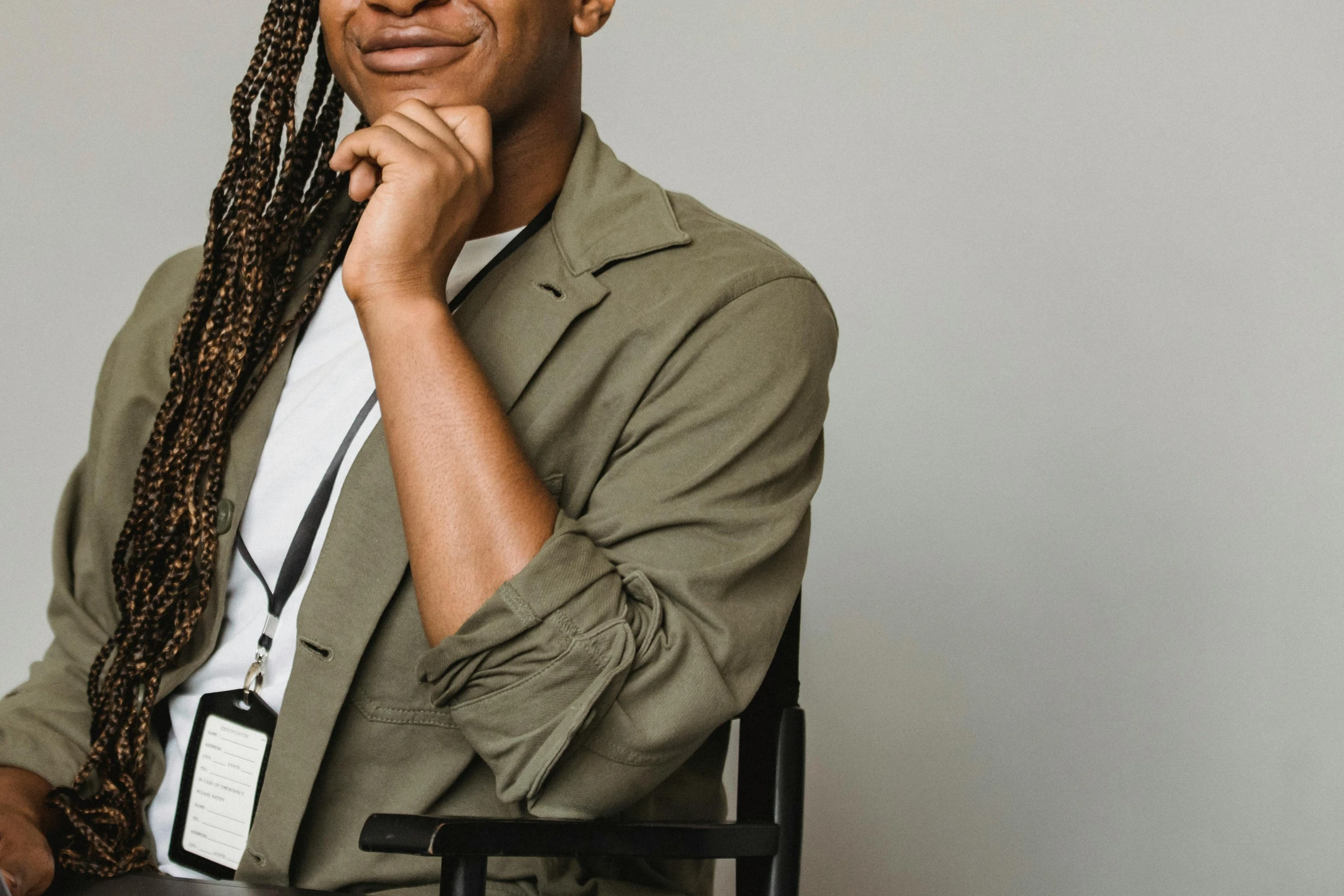 a man sitting in a chair with his hand on his chin, by Emma Andijewska, trending on pexels, black arts movement, nerdy black girl super hero, smiling slightly, woman with braided brown hair, wearing a worn out brown suit