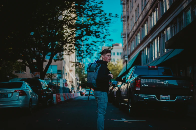 a man standing in the middle of a city street, by Carey Morris, pexels contest winner, a man wearing a backpack, underexposed grey, car shot, male teenager