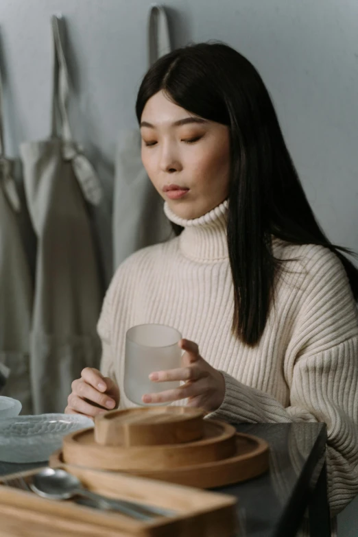 a woman sitting at a table holding a cup, inspired by Kim Tschang Yeul, trending on unsplash, renaissance, wearing turtleneck, cooking, glassware, slightly minimal