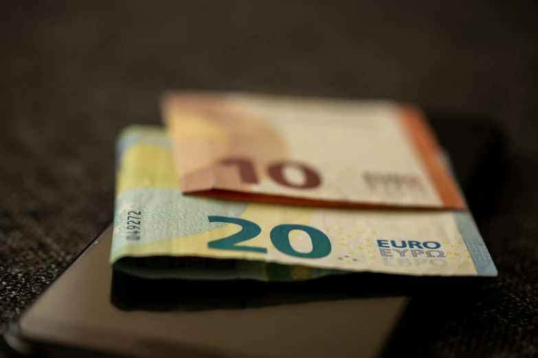 a cell phone sitting on top of a pile of euro bank notes, pexels, hyperrealism, paul barson, low quality photo, side - view, pair of keycards on table