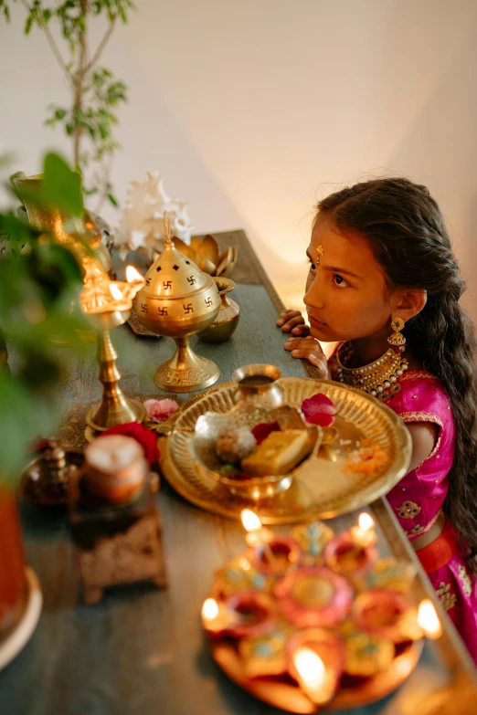 a little girl sitting at a table with a plate of food, hindu aesthetic, emitting light ornaments, gold, uplit