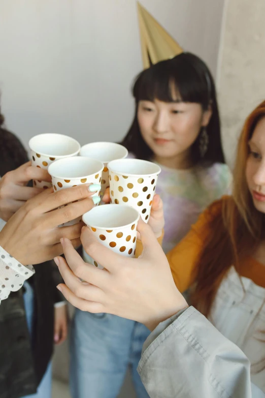 a group of women standing next to each other holding cups, by Ayami Kojima, trending on pexels, made of dots, white and gold, college party, japanese collection product