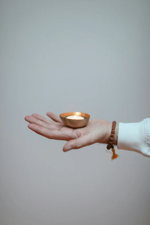 a person holding a lit candle in their hand, by Nina Hamnett, minimalism, ivory and copper, hindu stages of meditation, handcrafted, photograph taken in 2 0 2 0