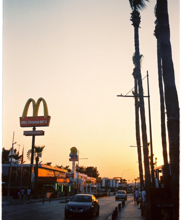 a couple of cars driving down a street next to tall palm trees, a polaroid photo, by Nathalie Rattner, unsplash, mcdonalds restaurant, sunset photo, terry richardson, mc donalds