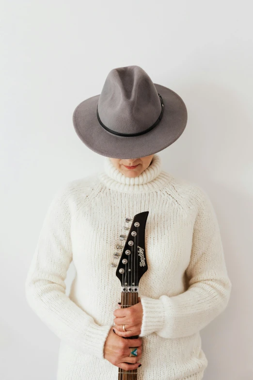 a woman wearing a hat and holding a guitar, an album cover, by Gavin Hamilton, pexels contest winner, grey sweater, white backround, wearing turtleneck, fedora