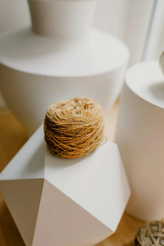 a couple of white vases sitting on top of a wooden table, an abstract sculpture, by Jessie Algie, unsplash, yarn ball, white and gold color scheme, detailed product image, dynamic angled shot