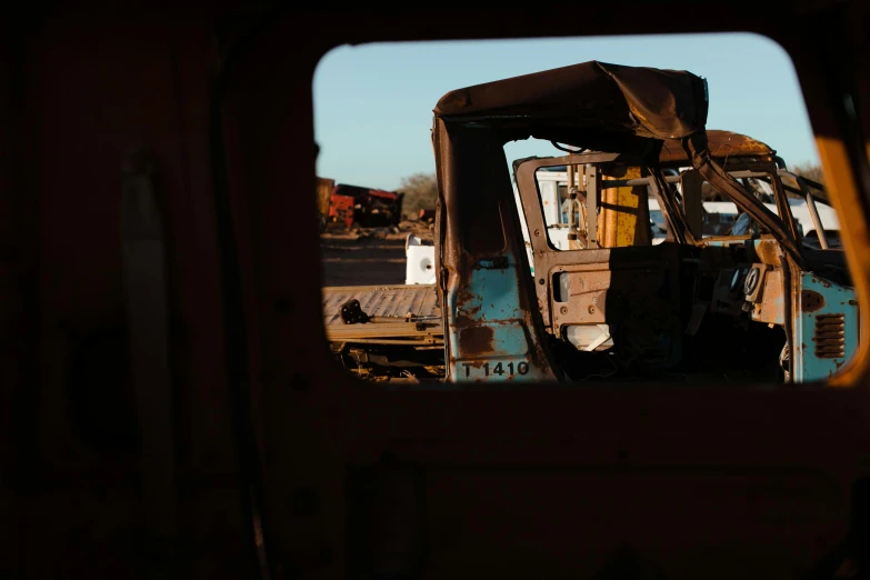 a truck that is sitting in the dirt, a portrait, unsplash, visual art, looking through a window frame, scrapyard, in the morning light, rear facing