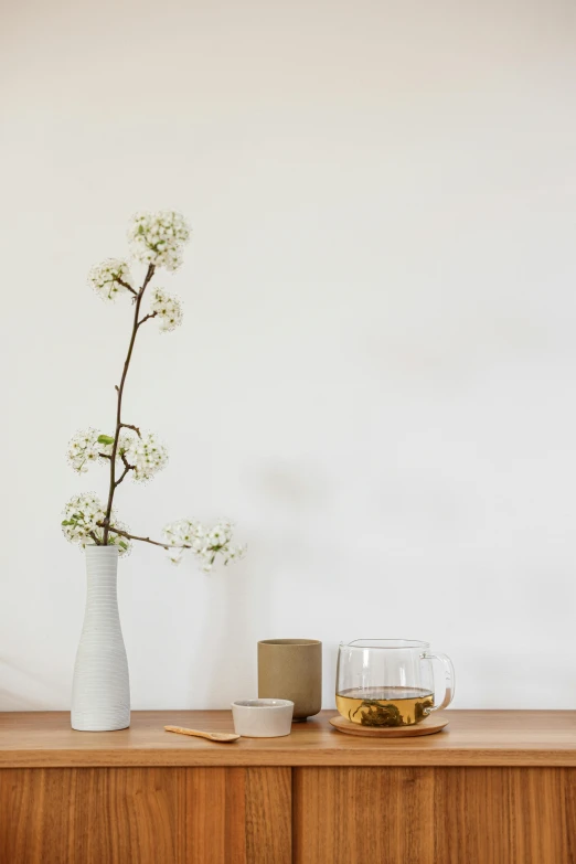 a white vase sitting on top of a wooden dresser, a still life, unsplash, minimalism, sakura season, glassware, ad image, dwell