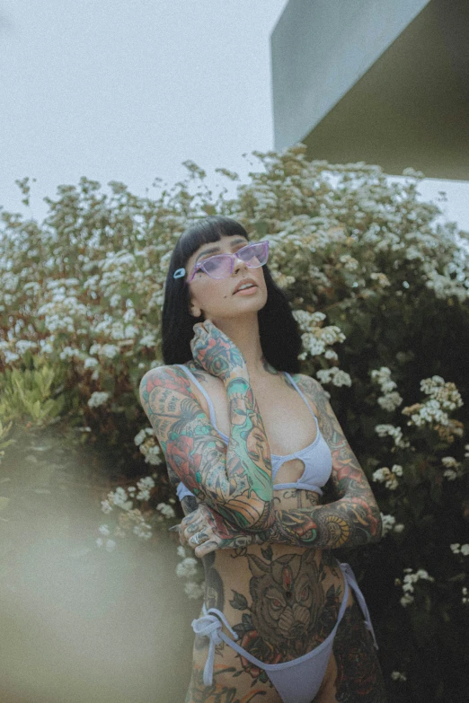 a woman with tattoos standing in front of a bush, implanted sunglasses, purple tint, high-quality photo, trending photo