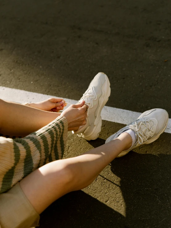 a woman sitting on the ground with her legs crossed, a picture, inspired by Elsa Bleda, trending on unsplash, wearing white sneakers, wavy hair spread out, light cream and white colors, rubber waffle outsole