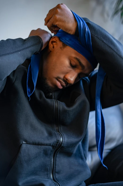 a man sitting on a couch with a blue tie around his head, trending on pexels, wearing a tracksuit, sleepy feeling, wearing a head scarf, crips