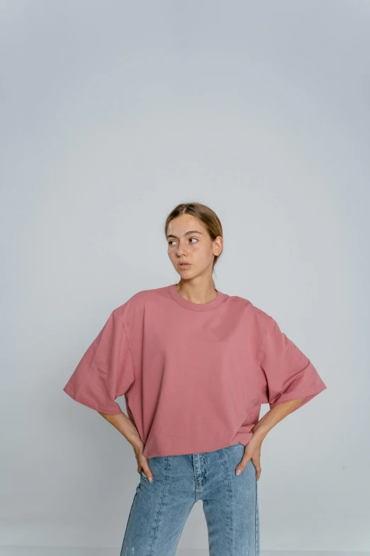 a woman standing with her hands in her pockets, unsplash contest winner, happening, pink shirt, cropped wide sleeve, non binary model, simple muted colors