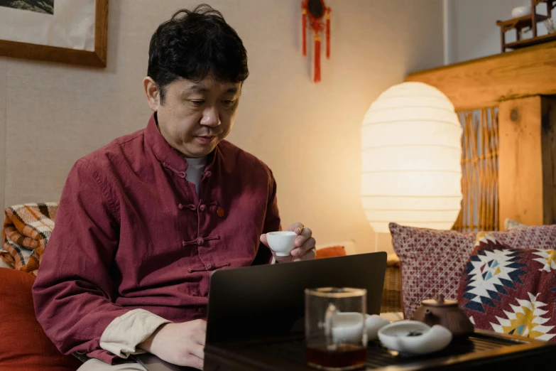 a man sitting on a couch using a laptop, a portrait, inspired by Chen Daofu, pexels contest winner, shin hanga, tea ceremony scene, avatar image, drinking tea, ethnicity : japanese