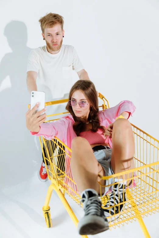 a man and a woman sitting in a shopping cart, by Julia Pishtar, trending on pexels, realism, yellow clothes, snapchat, pastel clothing, waist high