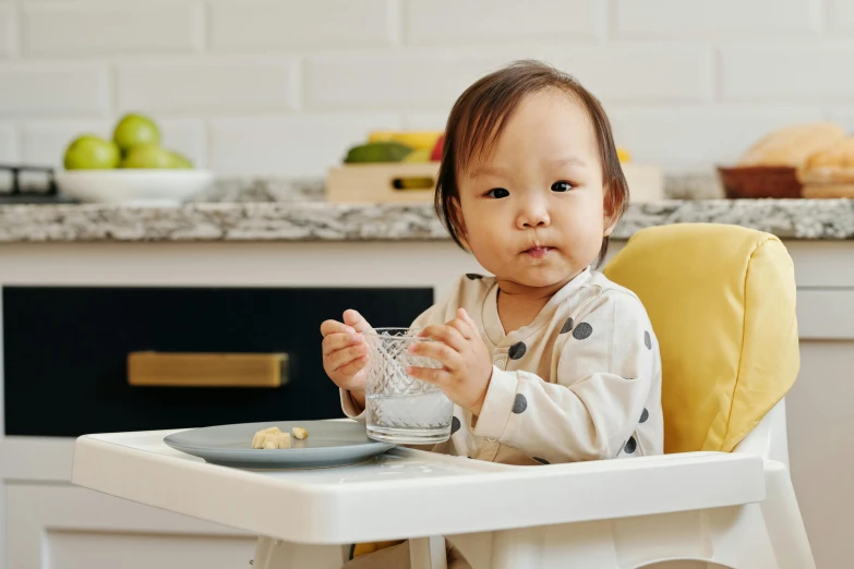 a baby sitting in a high chair eating food, pexels contest winner, jamie chung, looking straight to camera, grey, carrying a tray