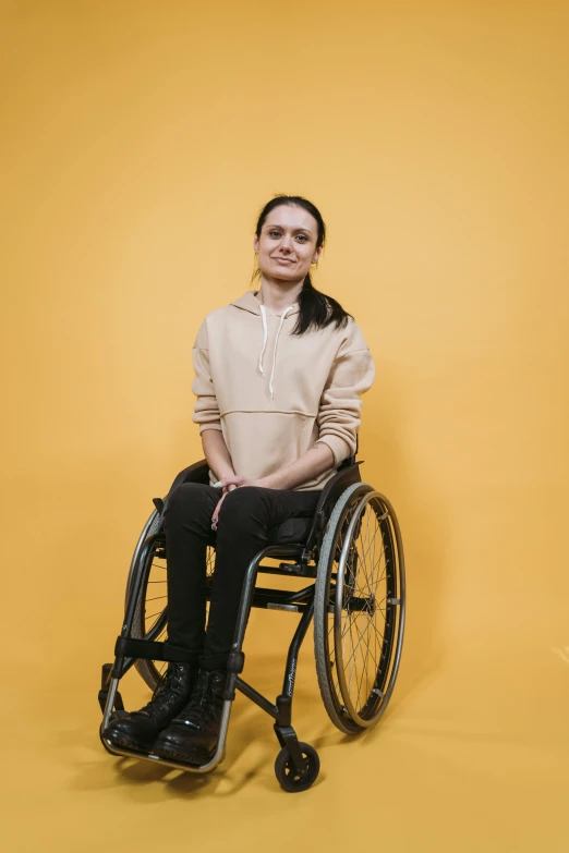 a woman in a wheelchair poses for a picture, an album cover, antipodeans, plain background, b - roll, yulia nevskaya, high resolution image