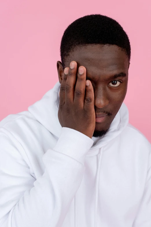 a man in a white hoodie covers his face with his hands, by Cosmo Alexander, trending on pexels, big pink eyes, solid background, ( ( dark skin ) ), yasuke 5 0 0 px models