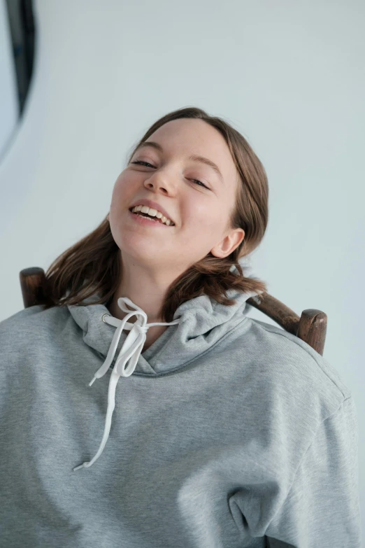 a woman sitting in a chair with her eyes closed, inspired by Jakob Gauermann, trending on unsplash, happening, wearing a grey hooded sweatshirt, happy fashion model face, portrait sophie mudd, smiling playfully