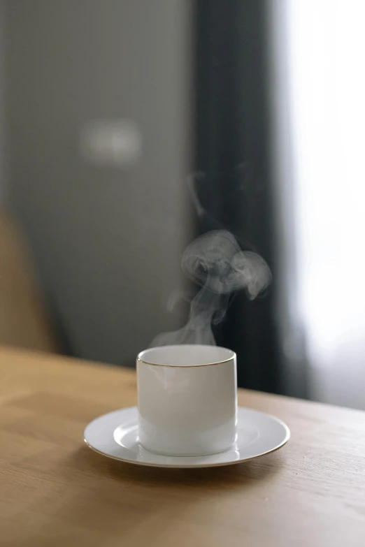 a cup of coffee sitting on top of a wooden table, emanating white smoke, at home, 王琛, grey