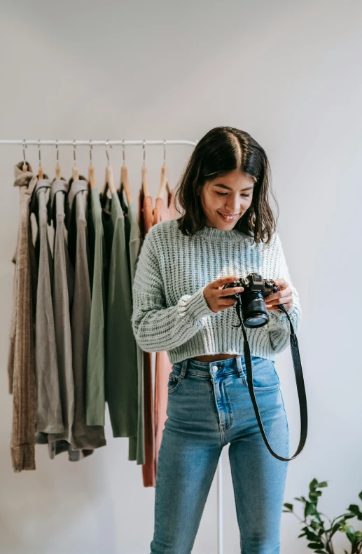 a woman standing in front of a rack of clothes holding a camera, trending on pexels, wearing casual sweater, product introduction photo