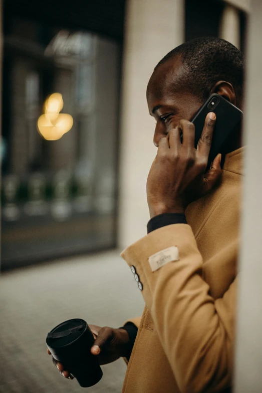 a man talking on a cell phone while holding a cup of coffee, by Andries Stock, trending on pexels, romanticism, muted brown yellow and blacks, wearing a turtleneck and jacket, dark skinned, heartbreak