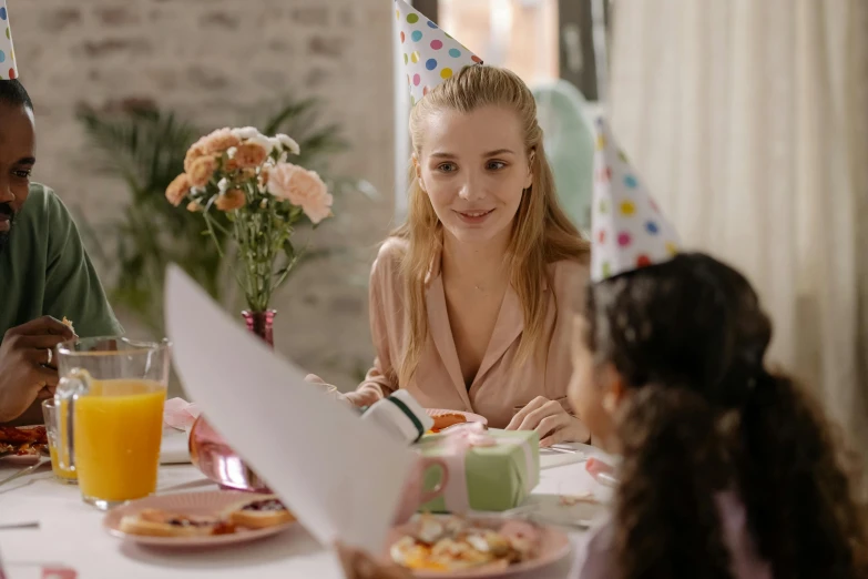 a group of people sitting at a table with plates of food, with a kid, wearing a party hat, gorgeous lady, abcdefghijklmnopqrstuvwxyz