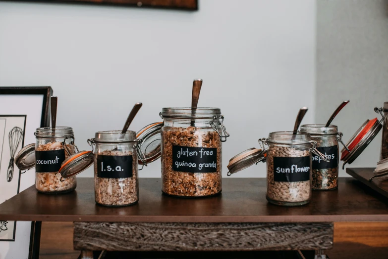 a wooden table topped with jars filled with food, by Emma Andijewska, pexels, cereal, product label, background image, breakfast buffet