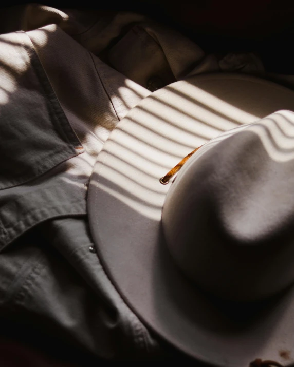 a white hat sitting on top of a bed, trending on pexels, deep shadows, impeccably dressed, pins of light, western clothing