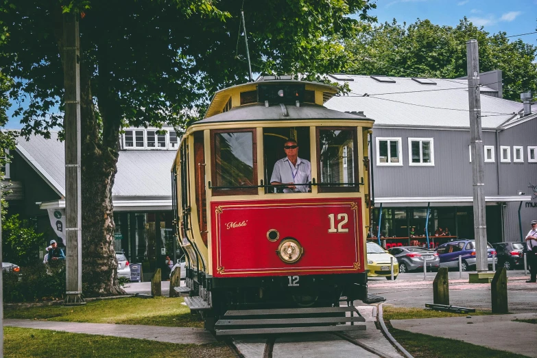 a red and yellow trolley traveling down a street, inspired by Tom Roberts, unsplash, te pae, handsome man, chairlifts, vintage car