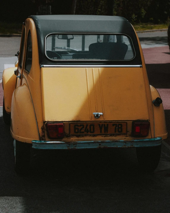 a small yellow car parked in a parking lot, by Daniël Mijtens, unsplash, historical photo, rear view, square, french