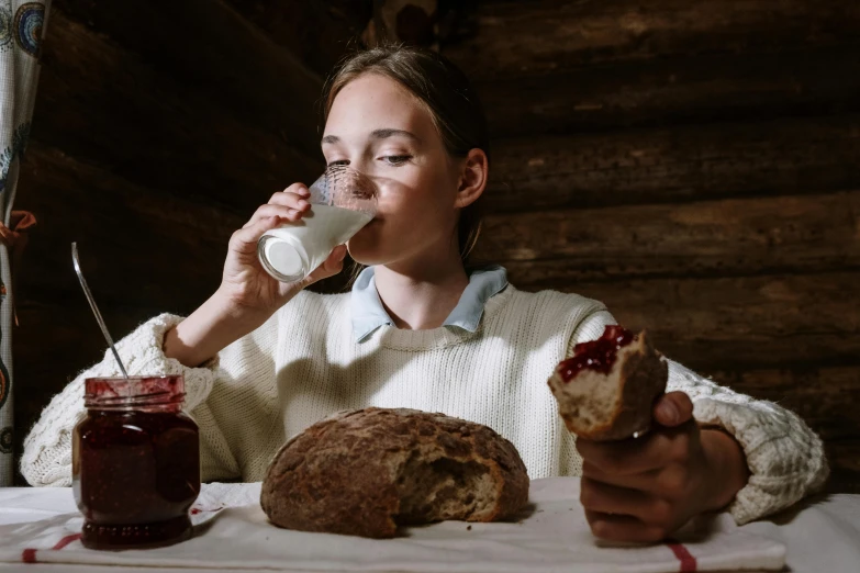 a woman sitting at a table drinking a glass of milk, inspired by Vasily Perov, pexels contest winner, bread, avatar image, 1 6 years old, in a cabin