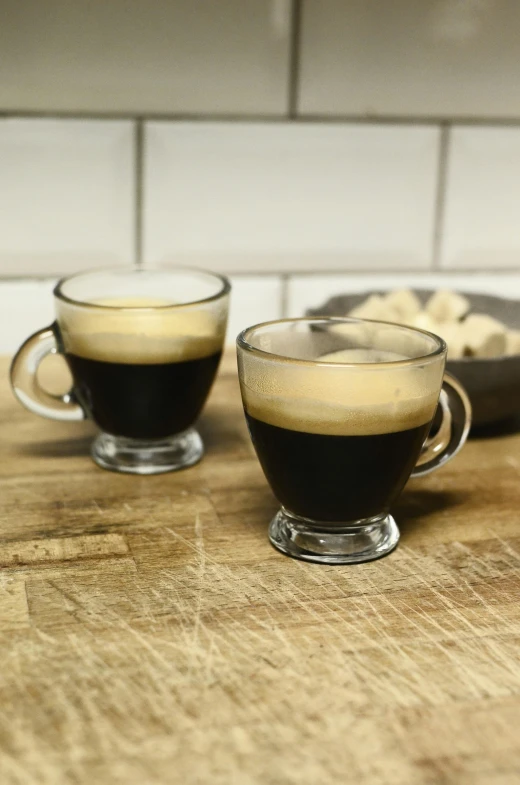 two cups of coffee sitting on top of a wooden table, with clear glass, irish, very award - winning, deep black