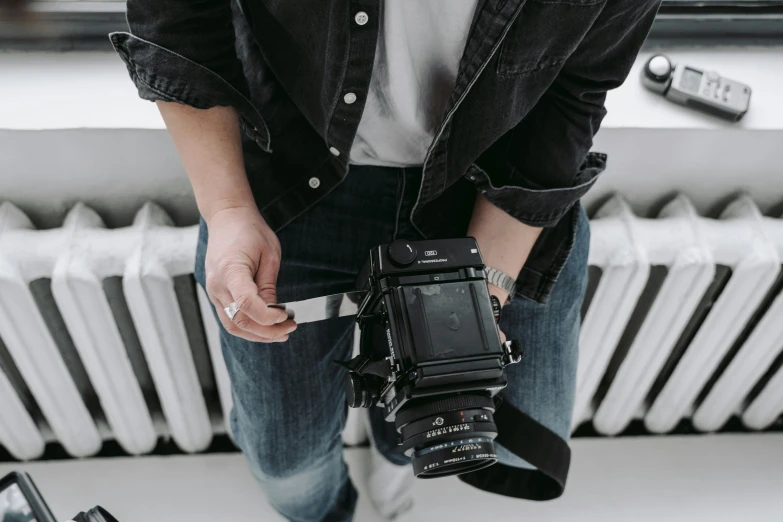 a man standing in front of a radiator holding a camera, hasselblad camera, wearing a dark shirt and jeans, unsplash transparent, holding arms on holsters